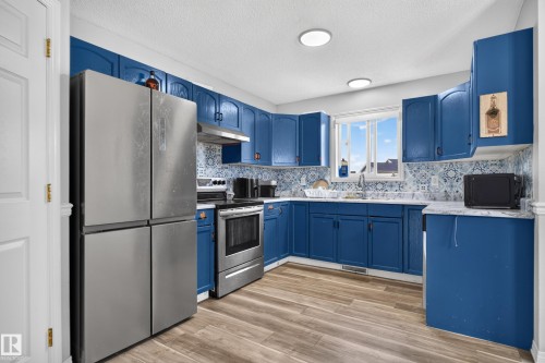 Kitchen featuring blue cabinetry, patterned tile backsplash, stainless steel appliances, wood-finish flooring, and recessed lighting - 3755 20 Street Nw, Edmonton, AB - Indoor Photo Showing Kitchen