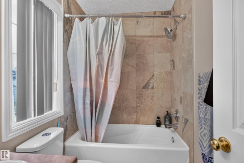 Bathtub with tile surround, a showerhead, and a window with vertical blinds - 3755 20 Street Nw, Edmonton, AB - Indoor Photo Showing Bathroom
