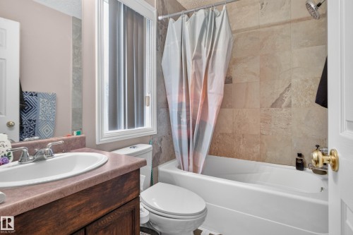 White bathtub with a rain shower head, tiled shower surround, and a wood-finish vanity with an integrated sink - 3755 20 Street Nw, Edmonton, AB - Indoor Photo Showing Bathroom