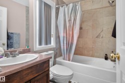 White bathtub with a rain shower head, tiled shower surround, and a wood-finish vanity with an integrated sink - 
