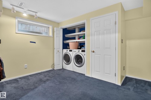 Laundry area with front-loading washer and dryer, built-in shelving, track lighting, and blue carpeting - 3755 20 Street Nw, Edmonton, AB - Indoor Photo Showing Laundry Room