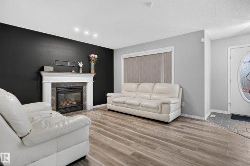 Wood-finish flooring, recessed ceiling lighting, fireplace with mantel and stone-finish surround, front entry door with decorative glass, and tiled entryway - 3755 20 Street Nw, Edmonton, AB - Indoor With Fireplace