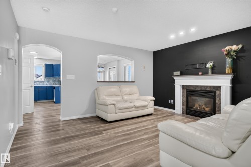Living area featuring wood-finish flooring, a fireplace with a white mantel and stone surround, and recessed lighting - 3755 20 Street Nw, Edmonton, AB - Indoor Photo Showing Living Room With Fireplace