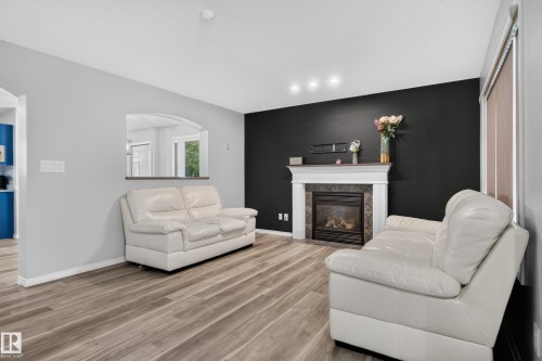 Fireplace with a white mantel and stone-tile surround, wood-finish flooring, recessed lighting, and an arched pass-through window - 3755 20 Street Nw, Edmonton, AB - Indoor Photo Showing Living Room With Fireplace