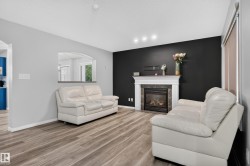 Fireplace with a white mantel and stone-tile surround, wood-finish flooring, recessed lighting, and an arched pass-through window - 