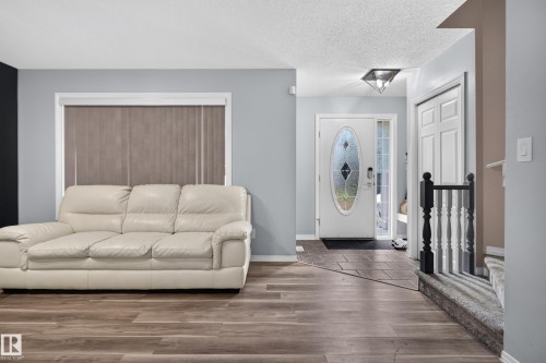 Wood-finish flooring throughout, light gray wall color, white trim, white front door with decorative glass inlay, and a black and white staircase railing - 3755 20 Street Nw, Edmonton, AB - Indoor