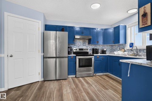 Kitchen featuring wood-finish flooring, blue cabinetry, stainless steel appliances, patterned tile backsplash, and recessed lighting - 3755 20 Street Nw, Edmonton, AB - Indoor Photo Showing Kitchen