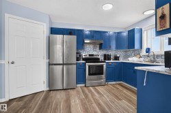 Kitchen featuring wood-finish flooring, blue cabinetry, stainless steel appliances, patterned tile backsplash, and recessed lighting - 