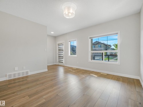 Wood-finish flooring, white walls, multiple windows, a ceiling-mounted light fixture, and a glass-paneled door - 203 Cavanagh Common Sw, Edmonton, AB - Indoor Photo Showing Other Room