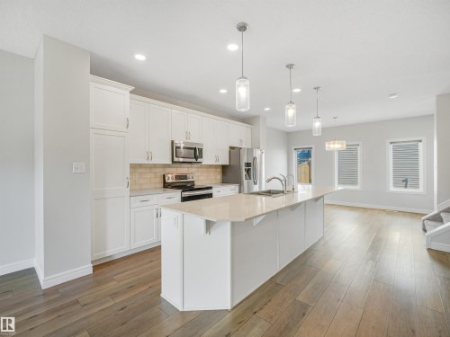 Gourmet kitchen with white cabinetry, light-toned countertops, tile backsplash, and stainless steel appliances - 203 Cavanagh Common Sw, Edmonton, AB - Indoor Photo Showing Kitchen With Upgraded Kitchen
