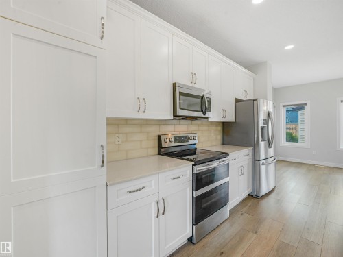 Kitchen featuring white cabinetry, stainless steel appliances, light-toned subway tile backsplash, light countertops, and wood-finish flooring - 203 Cavanagh Common Sw, Edmonton, AB - Indoor Photo Showing Kitchen