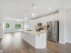 Open-concept kitchen featuring an island with sink, white shaker cabinets, stainless steel appliances, and light wood-finish flooring - 