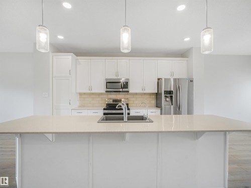 Modern kitchen featuring white cabinetry, stainless steel appliances including a refrigerator with ice and water dispensers, and a large quartz-topped island with seating - 203 Cavanagh Common Sw, Edmonton, AB - Indoor Photo Showing Kitchen With Upgraded Kitchen