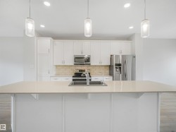 Modern kitchen featuring white cabinetry, stainless steel appliances including a refrigerator with ice and water dispensers, and a large quartz-topped island with seating - 