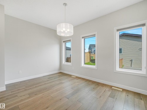Light-toned wood-finish flooring, white trim, and multiple windows - 203 Cavanagh Common Sw, Edmonton, AB - Indoor Photo Showing Other Room