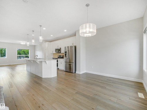 Open-concept living space with wood-finish flooring, a kitchen island, white cabinetry, and stainless steel appliances - 203 Cavanagh Common Sw, Edmonton, AB - Indoor Photo Showing Kitchen With Upgraded Kitchen