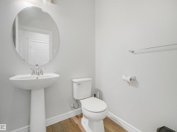 Pedestal sink with chrome faucet, oval mirror, toilet, and wood-finish flooring - 