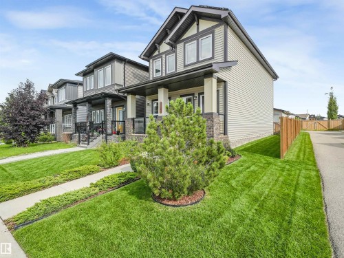Two-story residence with light-colored siding, a covered front porch, and dark trim accents - 203 Cavanagh Common Sw, Edmonton, AB - Outdoor