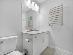 White vanity with integrated sink, rectangular mirror, brushed nickel light fixture, and wall-mounted towel warmer - 