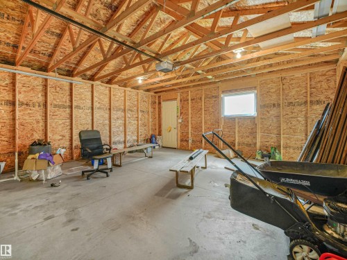 Spacious garage with exposed wood trusses, concrete flooring, and a single window - 203 Cavanagh Common Sw, Edmonton, AB - Indoor Photo Showing Basement