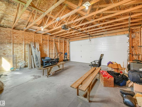 Spacious garage with exposed wood trusses, concrete flooring, plywood walls, and a white overhead door - 203 Cavanagh Common Sw, Edmonton, AB - Indoor Photo Showing Garage