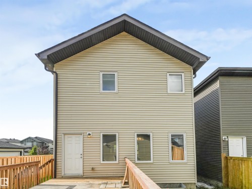 Two-story exterior with horizontal siding, multiple windows, a white entry door, and an attached wood deck - 203 Cavanagh Common Sw, Edmonton, AB - Outdoor With Exterior