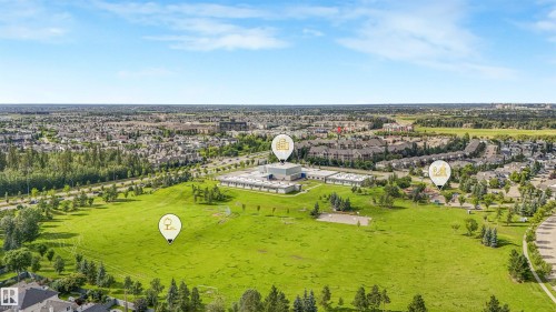 Expansive green space bordered by residential buildings and mature trees - 203 Cavanagh Common Sw, Edmonton, AB - Outdoor With View
