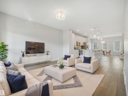 Open-concept living area featuring light wood-finish flooring, recessed lighting, and a kitchen with white cabinetry, stainless steel appliances, and a central island - 