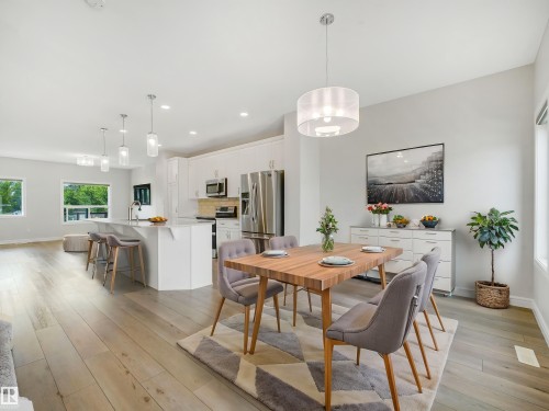 Light wood-finish flooring, white cabinetry, stainless steel appliances, and an expansive kitchen island with pendant lighting - 203 Cavanagh Common Sw, Edmonton, AB - Indoor Photo Showing Dining Room
