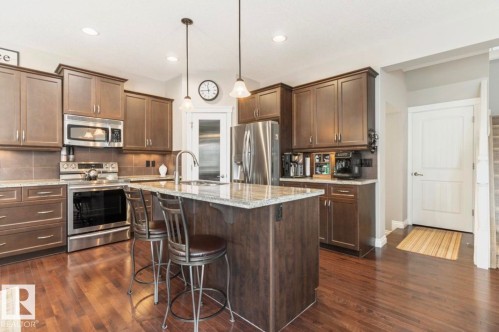 Kitchen featuring rich wood-finish flooring, dark wood cabinetry, granite countertops, and stainless steel appliances - 22 Voleta Crest, Spruce Grove, AB - Indoor Photo Showing Kitchen With Stainless Steel Kitchen With Upgraded Kitchen