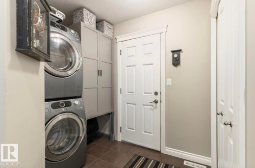 Dedicated laundry area featuring stacked front-load washer and dryer, tile flooring, and integrated storage cabinetry - 22 Voleta Crest, Spruce Grove, AB - Indoor Photo Showing Laundry Room