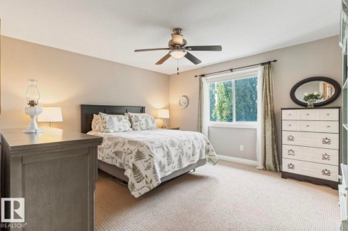 Spacious room featuring neutral wall tones, a ceiling fan with integrated lighting, a large window with white trim, and light-toned carpet flooring - 22 Voleta Crest, Spruce Grove, AB - Indoor Photo Showing Bedroom