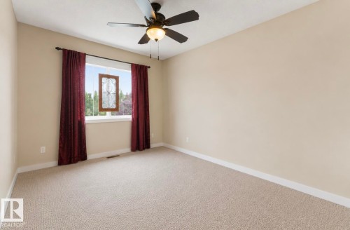 Neutral tone walls featuring a window with decorative leaded glass, a ceiling fan with light fixture, and textured carpeting - 22 Voleta Crest, Spruce Grove, AB - Indoor Photo Showing Other Room