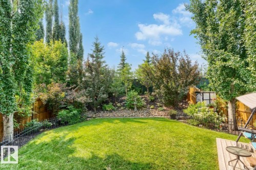 Expansive backyard featuring a lush lawn, mature trees, tiered landscaping, and a dark metal fence - 22 Voleta Crest, Spruce Grove, AB - Outdoor