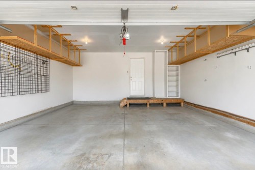 Spacious garage with concrete flooring, overhead wood shelving, a built-in storage unit, and a pegboard wall system - 22 Voleta Crest, Spruce Grove, AB - Indoor Photo Showing Garage