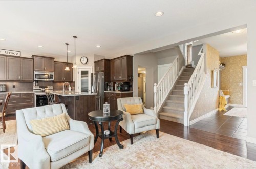 Open-concept living space with dark wood-finish flooring, a kitchen featuring dark cabinetry and stainless steel appliances, and a carpeted staircase with white railings - 22 Voleta Crest, Spruce Grove, AB - Indoor