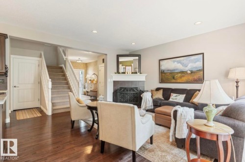 Living area featuring dark wood-finish flooring, a carpeted staircase with white railings, a fireplace with a dark tile surround and white mantel, and recessed lighting - 22 Voleta Crest, Spruce Grove, AB - Indoor Photo Showing Living Room With Fireplace