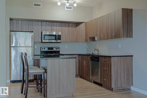 Kitchen featuring wood-finish cabinetry, stainless steel appliances, dark countertops, and an island with bar seating - #607 10518 113 St Nw Nw, Edmonton, AB - Indoor Photo Showing Kitchen With Stainless Steel Kitchen
