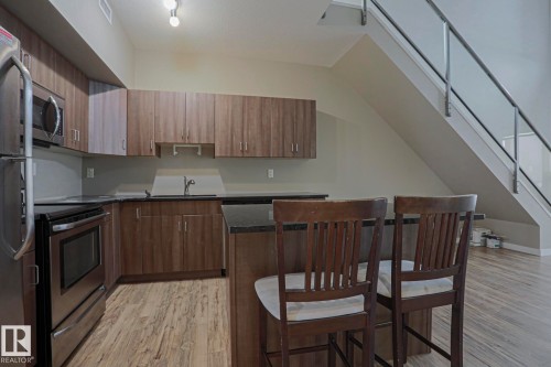 Kitchen featuring wood-finish cabinetry, stainless steel appliances, dark countertops, and wood-finish flooring - #607 10518 113 St Nw Nw, Edmonton, AB - Indoor Photo Showing Kitchen