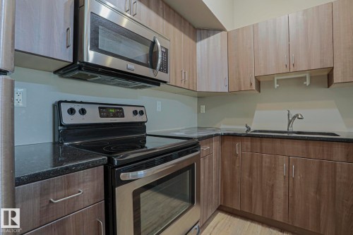 Kitchen featuring wood-finish cabinetry, dark countertops, a stainless steel microwave, and a black range - #607 10518 113 St Nw Nw, Edmonton, AB - Indoor Photo Showing Kitchen