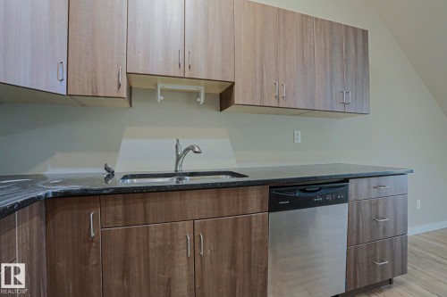 Wood-finish cabinetry with stainless steel hardware, dark countertop, stainless steel sink with a gooseneck faucet, and a built-in stainless steel dishwasher - #607 10518 113 St Nw Nw, Edmonton, AB - Indoor Photo Showing Kitchen With Double Sink