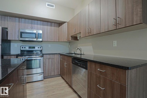 Kitchen featuring wood-finish cabinetry, stainless steel appliances, dark countertops, and wood-look flooring - #607 10518 113 St Nw Nw, Edmonton, AB - Indoor Photo Showing Kitchen With Stainless Steel Kitchen