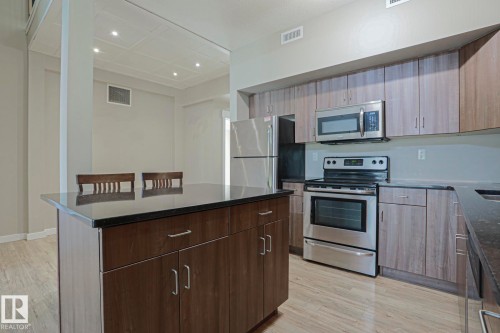 Kitchen featuring dark countertops, wood-finish cabinetry, stainless steel appliances, and an integrated island with additional storage - #607 10518 113 St Nw Nw, Edmonton, AB - Indoor Photo Showing Kitchen With Stainless Steel Kitchen