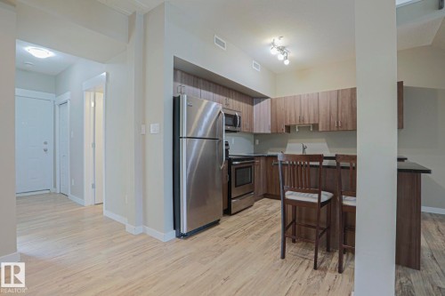 Kitchen featuring stainless steel appliances, wood-finish cabinetry, and a breakfast bar with dark countertops - #607 10518 113 St Nw Nw, Edmonton, AB - Indoor Photo Showing Kitchen