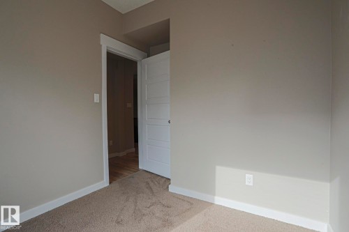Neutral wall color, wall-to-wall carpeting, white trim, paneled interior door, wood-finish flooring visible through doorway - #607 10518 113 St Nw Nw, Edmonton, AB - Indoor Photo Showing Other Room
