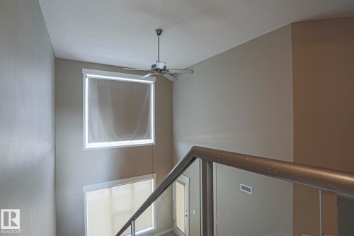 Two-story ceiling with a ceiling fan, two windows with roller shades, and a metal and glass railing system - #607 10518 113 St Nw Nw, Edmonton, AB - Indoor Photo Showing Other Room