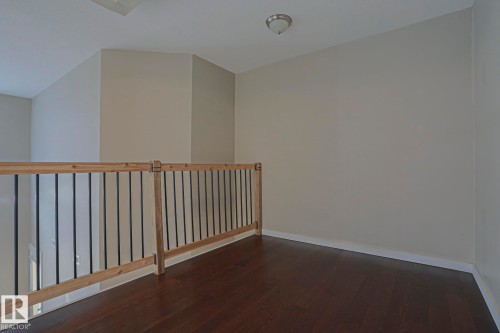 Dark wood-finish flooring with light wood banister and black metal balusters - #607 10518 113 St Nw Nw, Edmonton, AB - Indoor Photo Showing Other Room
