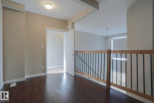 Dark wood-finish flooring, light tan wall color, wood and metal baluster railing, flush mount ceiling lighting, and a ceiling fan - #607 10518 113 St Nw Nw, Edmonton, AB - Indoor Photo Showing Other Room