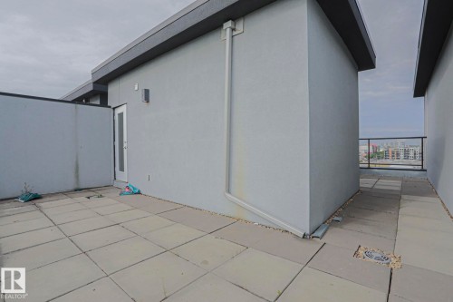 Tiled patio area with a glass-paneled railing, exterior wall-mounted lighting, and a modern flat roofline - #607 10518 113 St Nw Nw, Edmonton, AB - Outdoor With Exterior