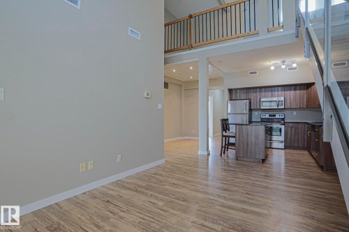 High ceilings, wood-finish flooring, kitchen island, stainless steel appliances, and a loft space with a black railing - #607 10518 113 St Nw Nw, Edmonton, AB - Indoor Photo Showing Other Room